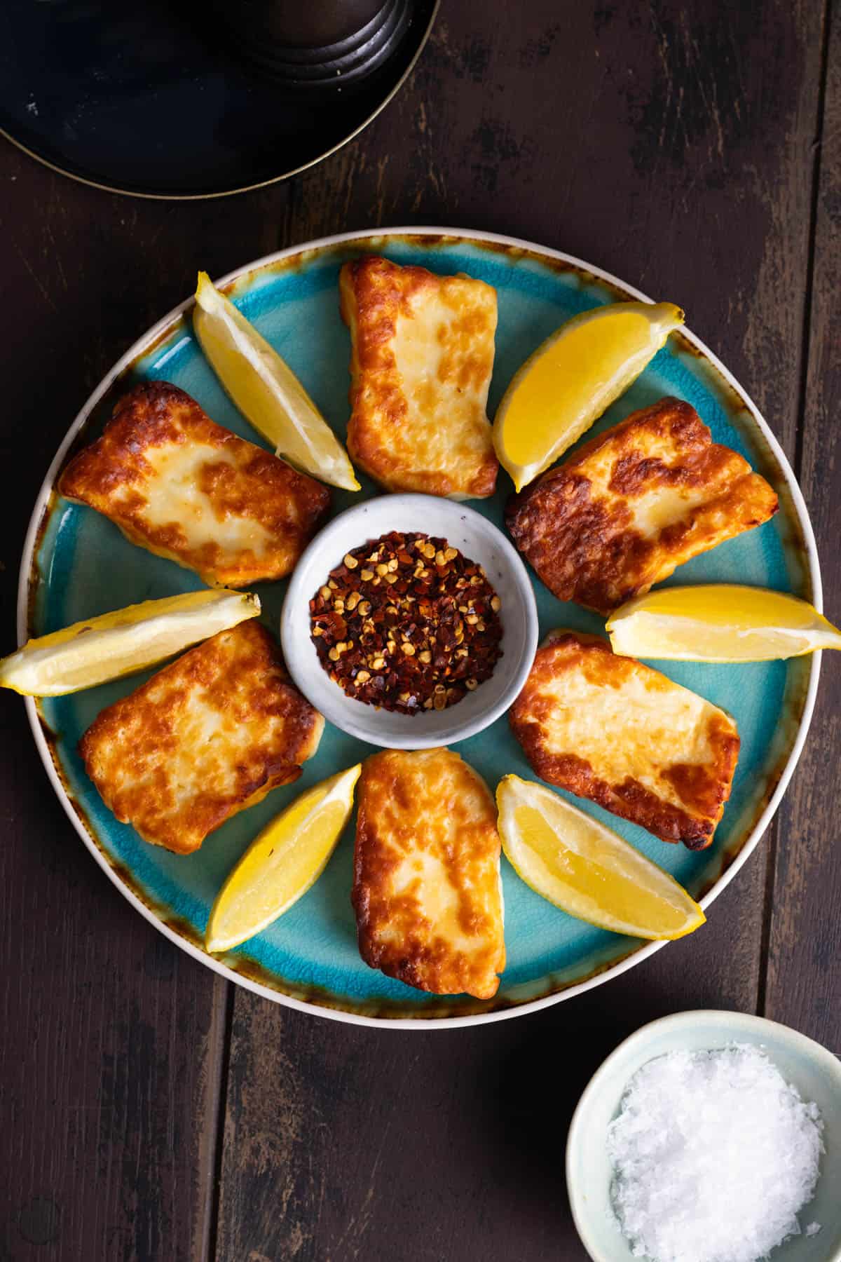 Air fried halloumi on a blue plate with lemon wedges and chili flakes.