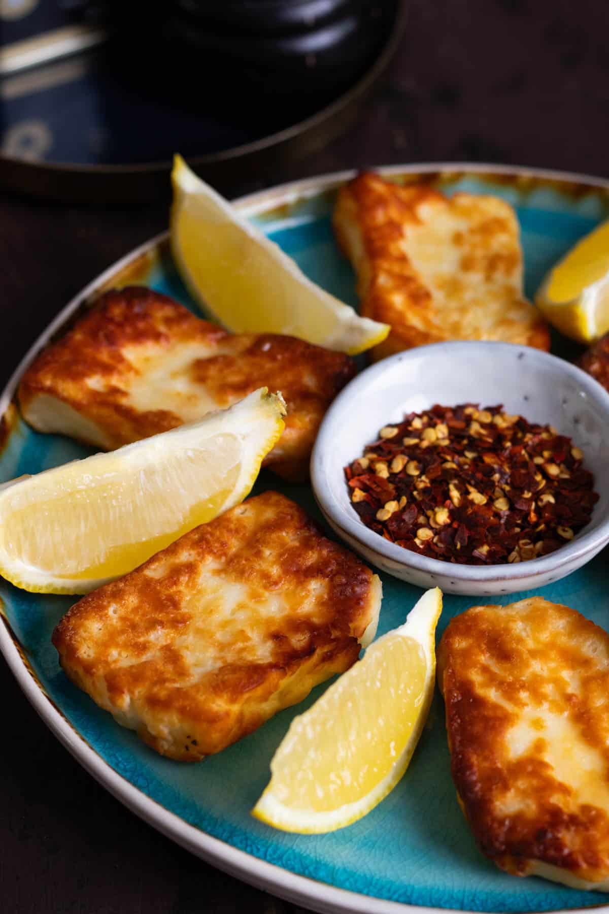 Air fried halloumi on a blue plate with lemon wedges and chili flakes.