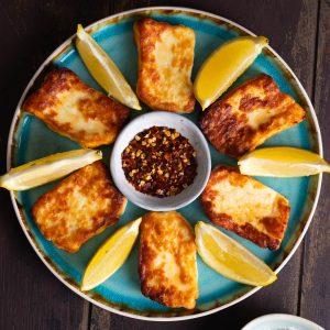 Air fried halloumi on a blue plate with lemon wedges and chili flakes.