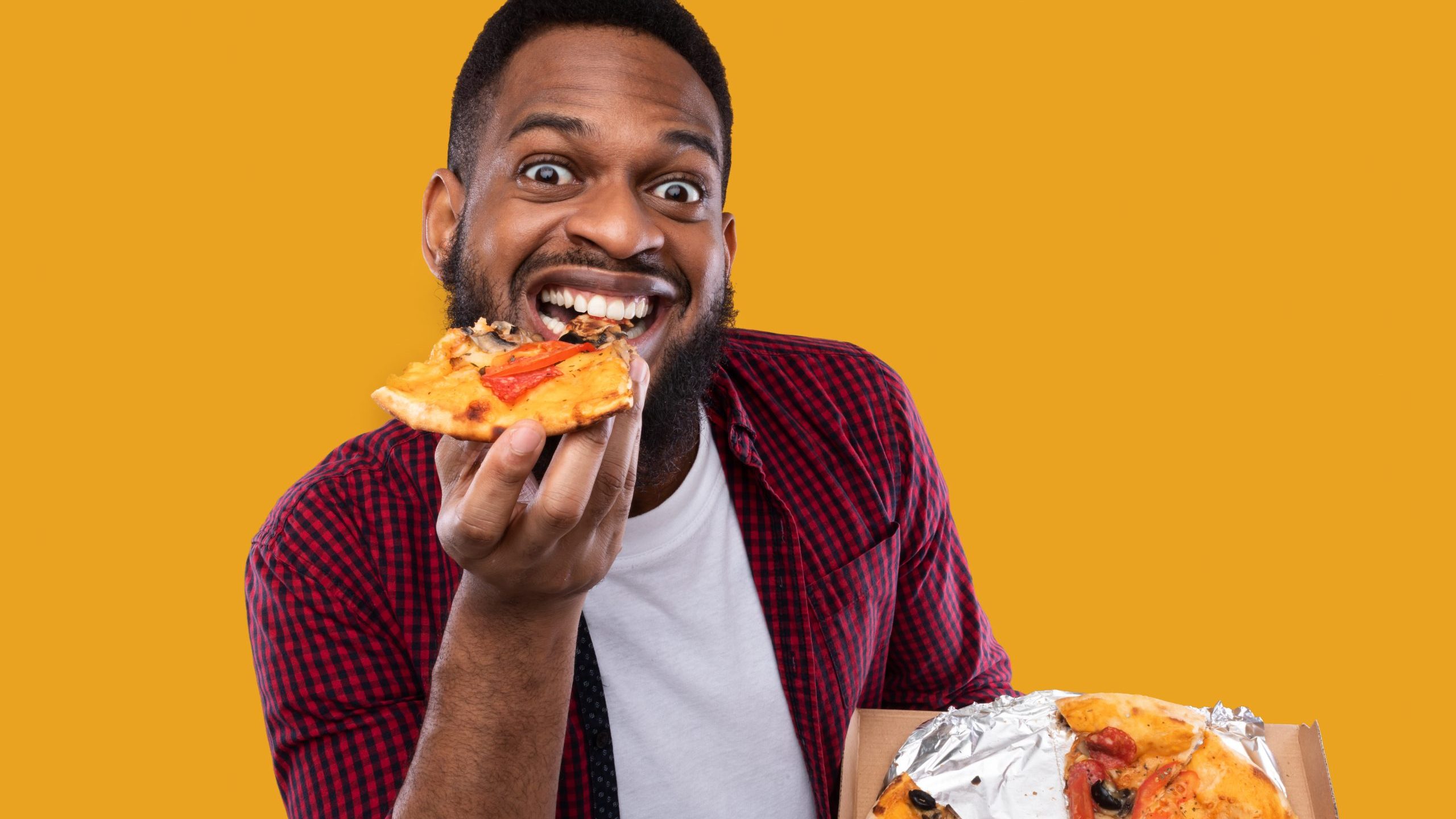 A man eating a slice of pizza while holding the rest of the pizza in one hand.