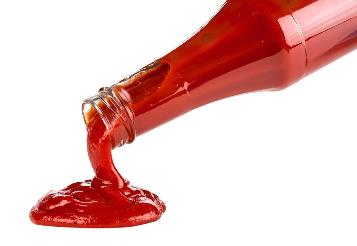 A bottle of ketchup with ketchup being poured out of it.