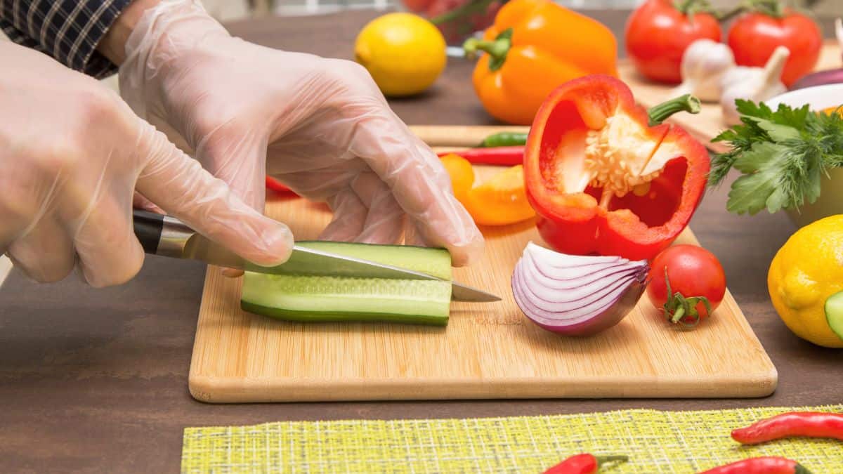 A person wearing plastic gloves slicing cucumber.