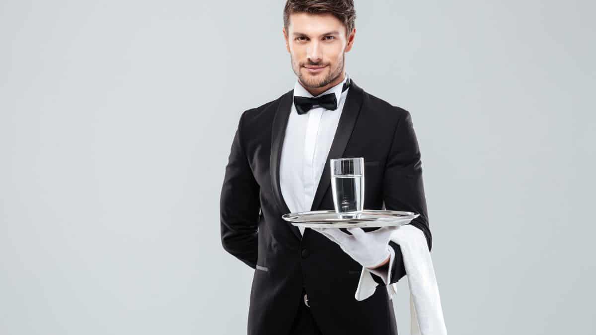 A man in a tuxedo serving a glass of water.