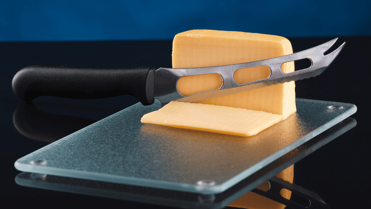 Cheese and a knife on a glass cutting board.