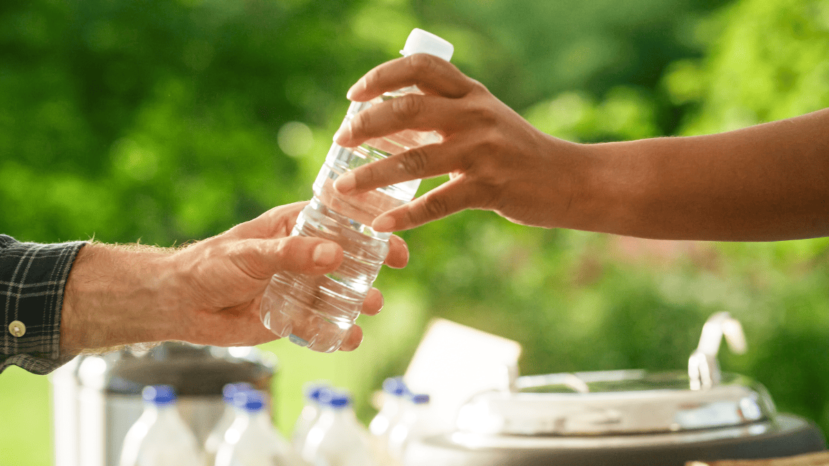 A person handing a water bottle to another person.