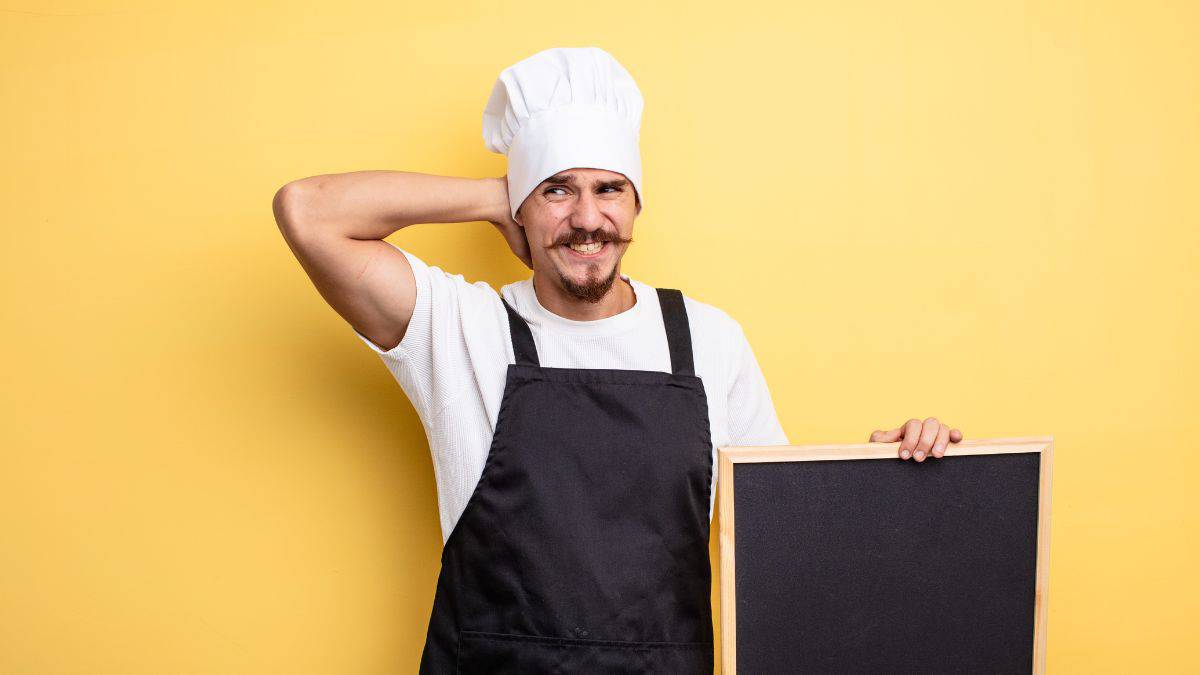 A man with a chef's hat and a blackboard.