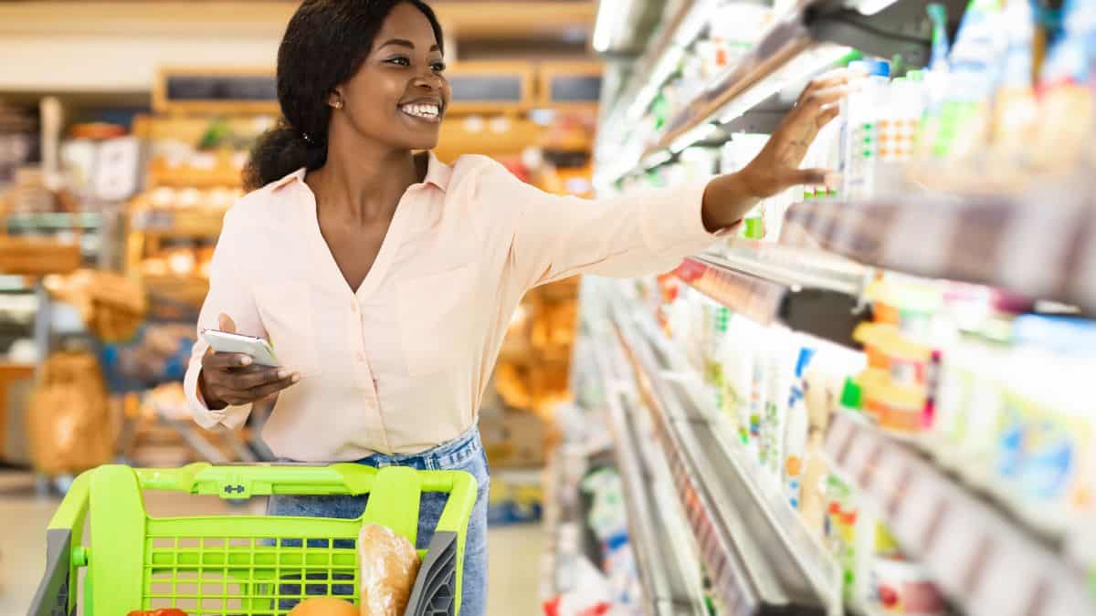A woman shopping in a grocery store with her phone in her hand.