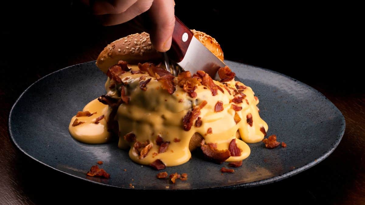 Cutting into a burger loaded with melted cheese and bacon.