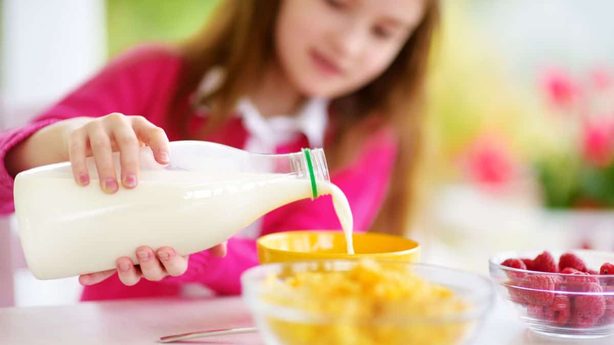 A girl pouring milk into a bowl.
