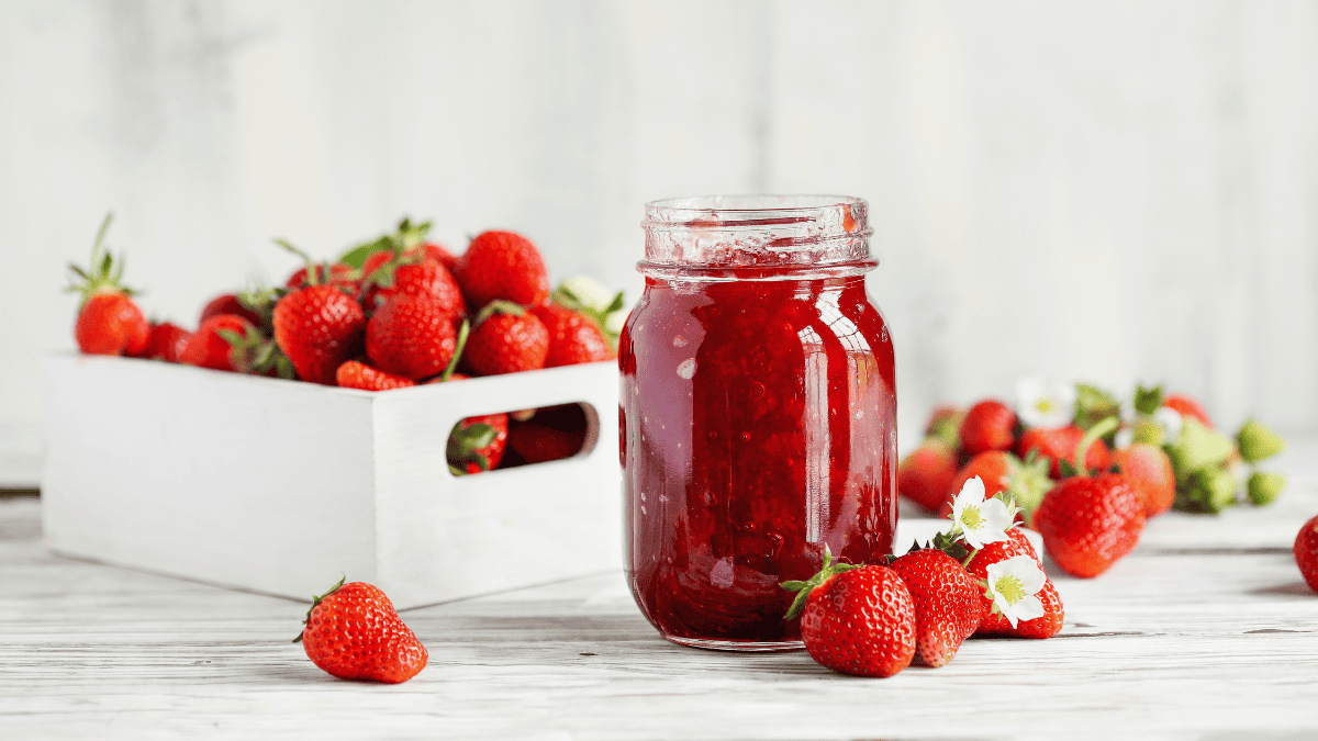 A jar of strawberry jam surrounded by strawberries.