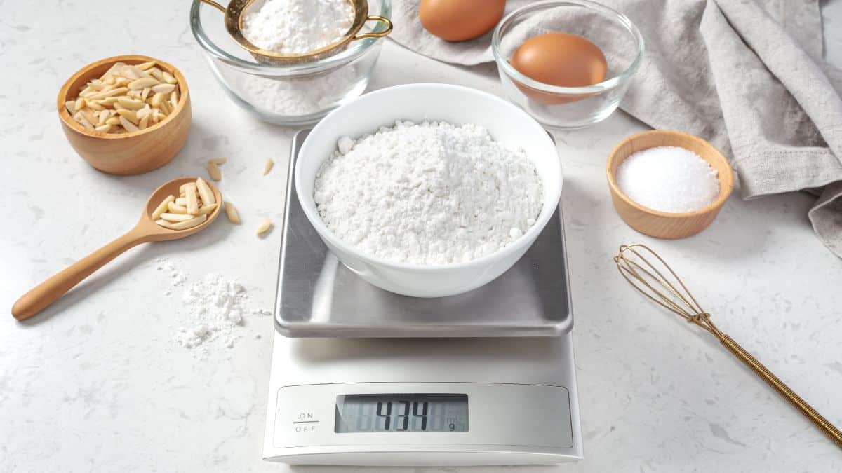 A bowl of flour being weighed on a kitchen scale.