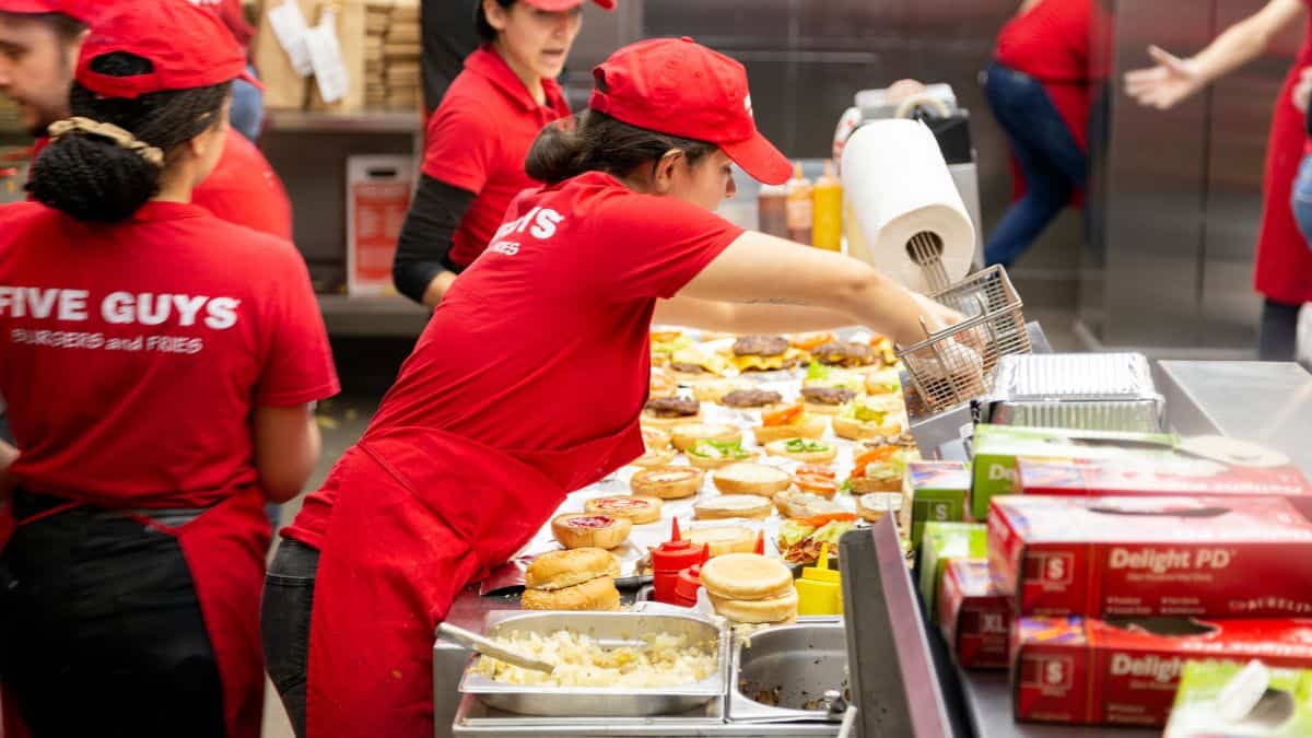 People working in the kitchen at a five guys restaurant.