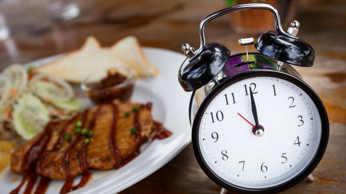 An old fashioned alarm clock next to a plate of food.