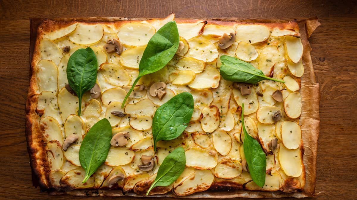 A potato pizza topped with green leaves.