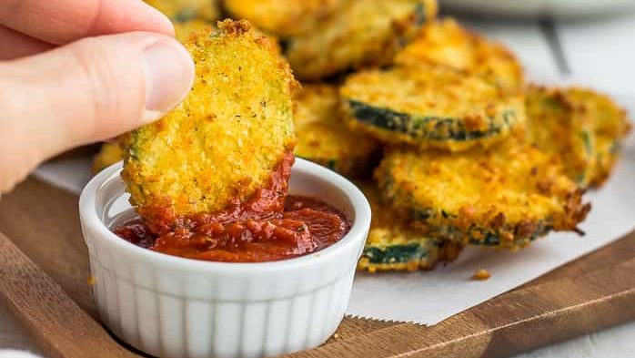 A zucchini chip being dipped in a red sauce.