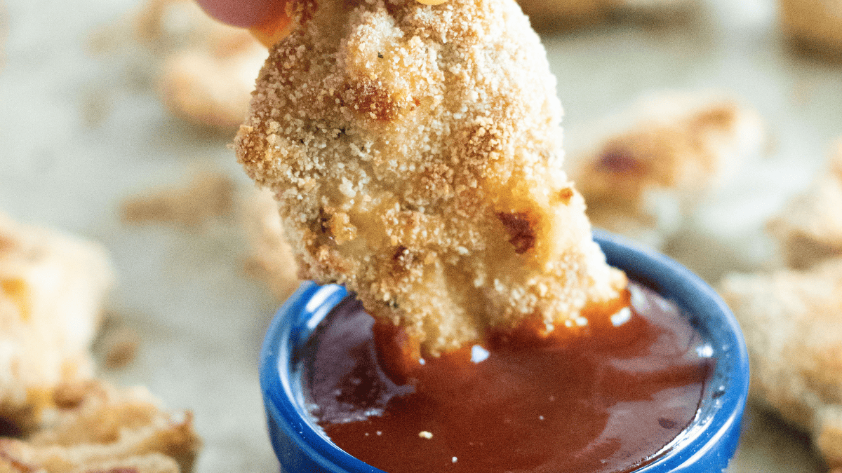 A baked chicken tender being dipped in red sauce.