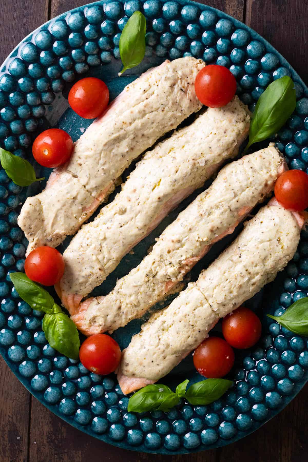 Pesto salmon on a serving platter with cherry tomatoes and fresh basil.