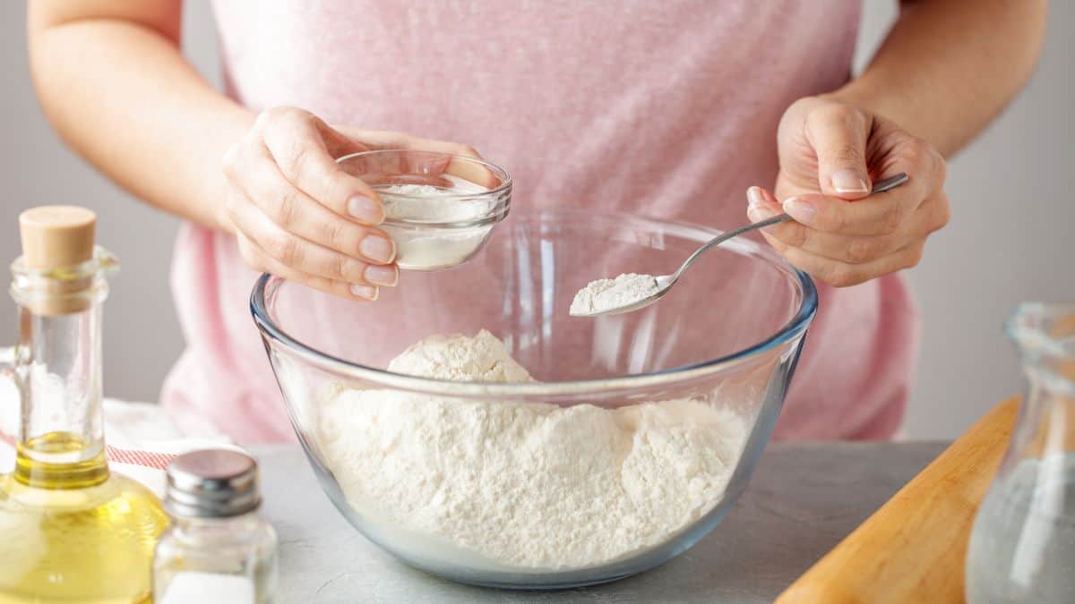 A woman adding baking powder to flour.