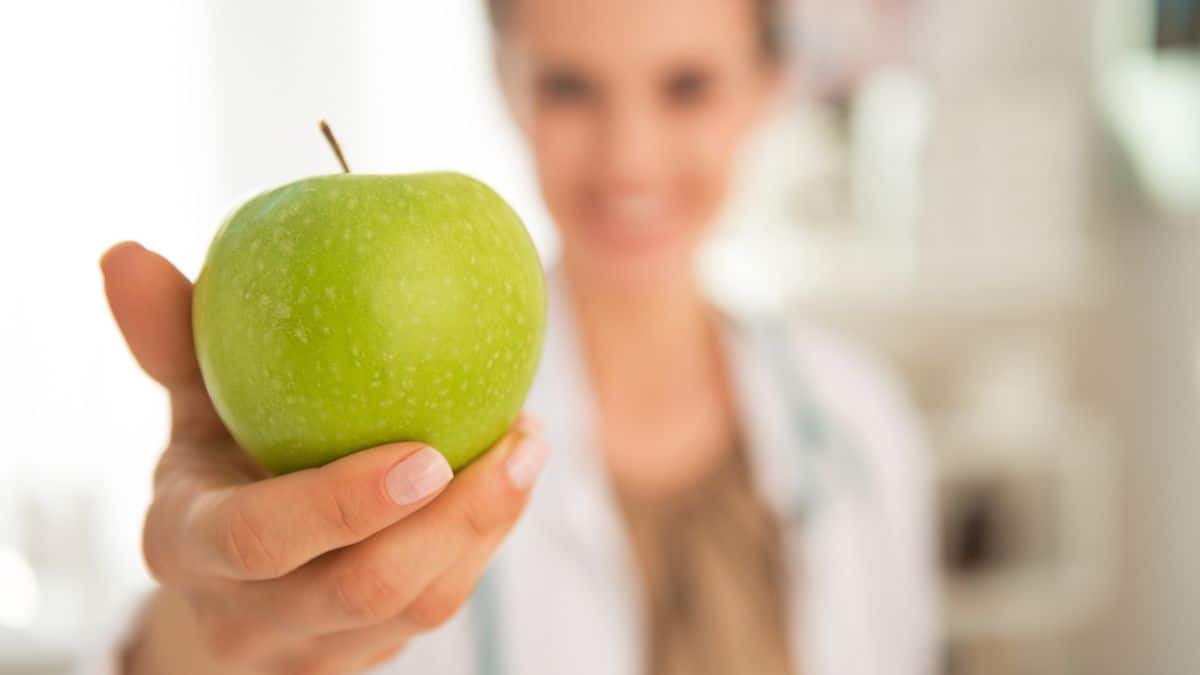 A woman in a white coat holding up a green apple.