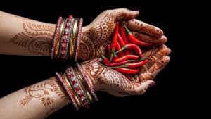 A woman with henna tattoos holding chilies in her hands.