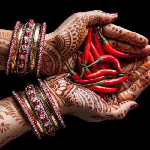 A woman with henna tattoos holding chilies in her hands.