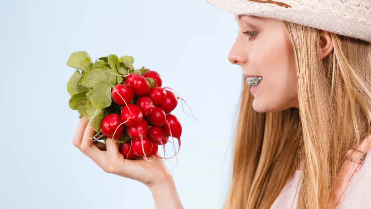 A girl with braces holding radishes.