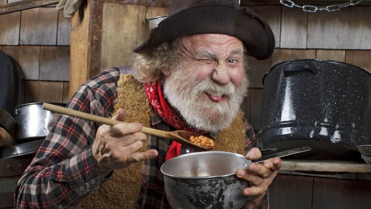 An old man eating beans straight from the pot.