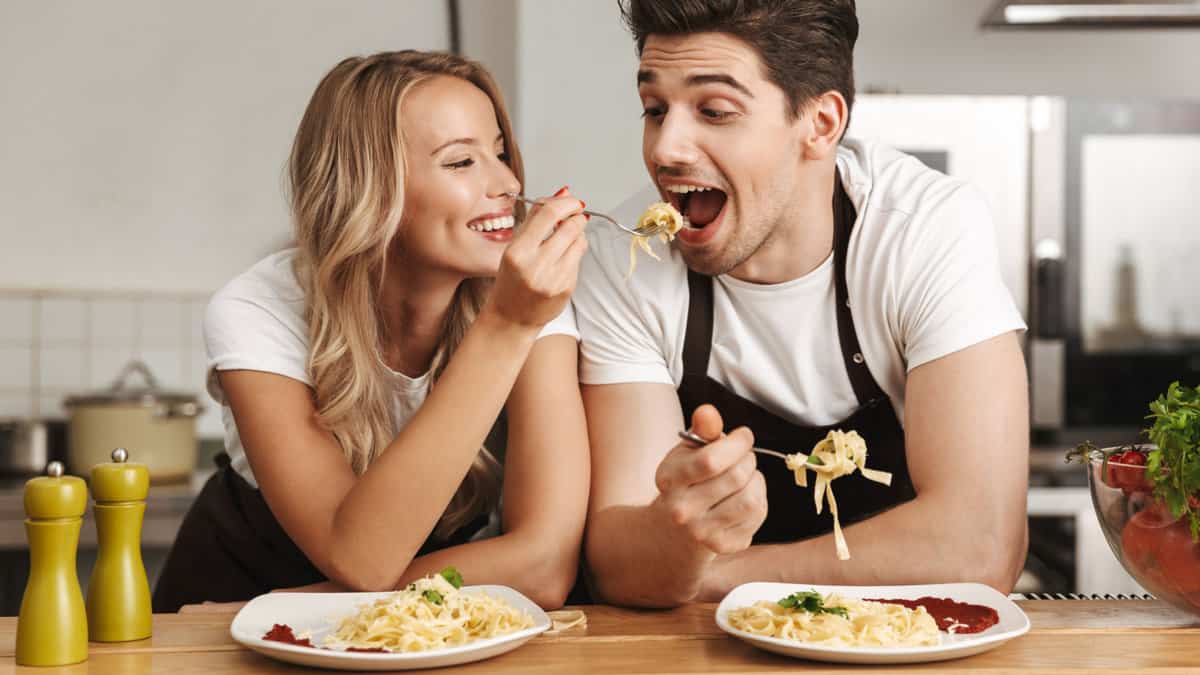 Happy woman feeding a man pasta.