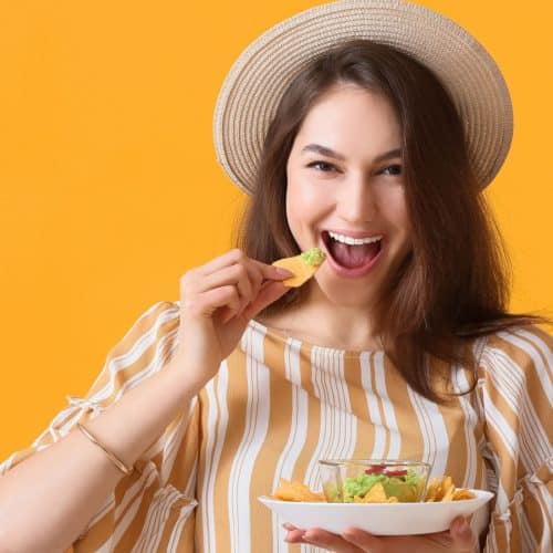 A woman eating chips with guacamole.