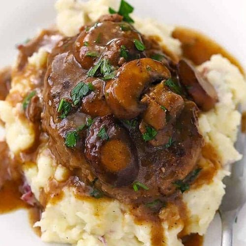 A plate with mashed potatoes and salisbury steak.