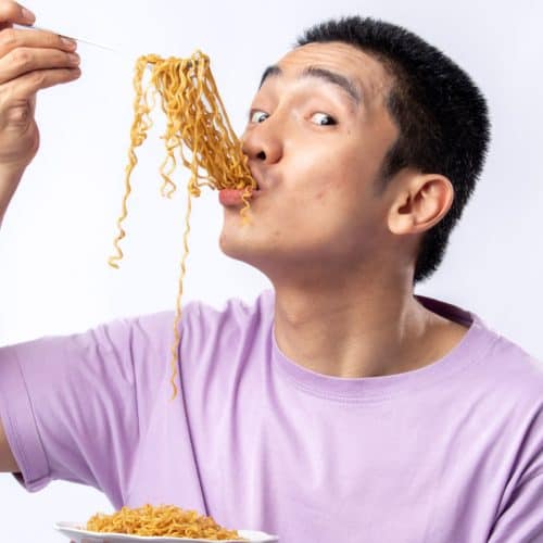 An Asian man eating noodles.