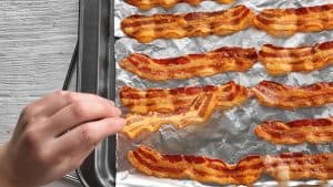 Crispy bacon baked on a baking sheet, with a hand picking up one piece.