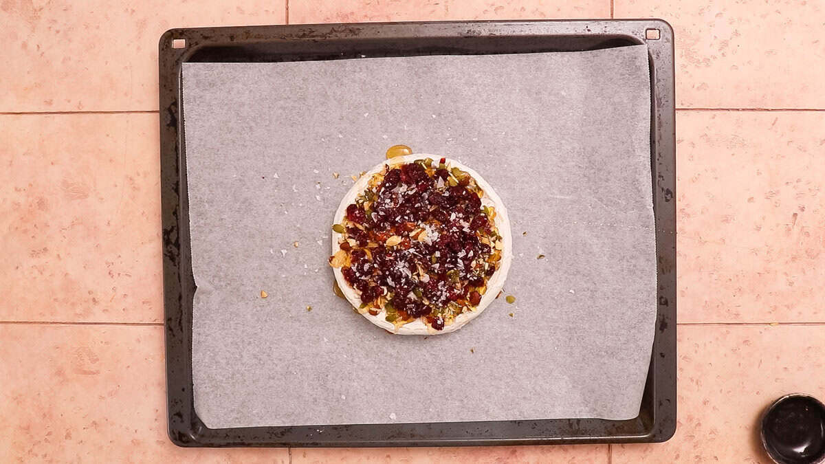A brie cheese topped with nuts and dried fruits before baking.