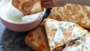 A buffalo chicken quesadilla being dipped in blue cheese sauce.