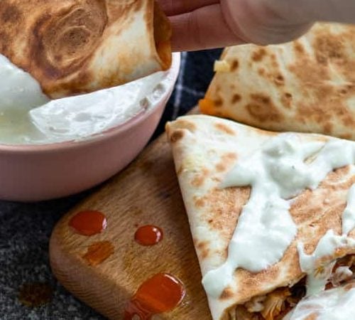 A buffalo chicken quesadilla being dipped in blue cheese sauce.