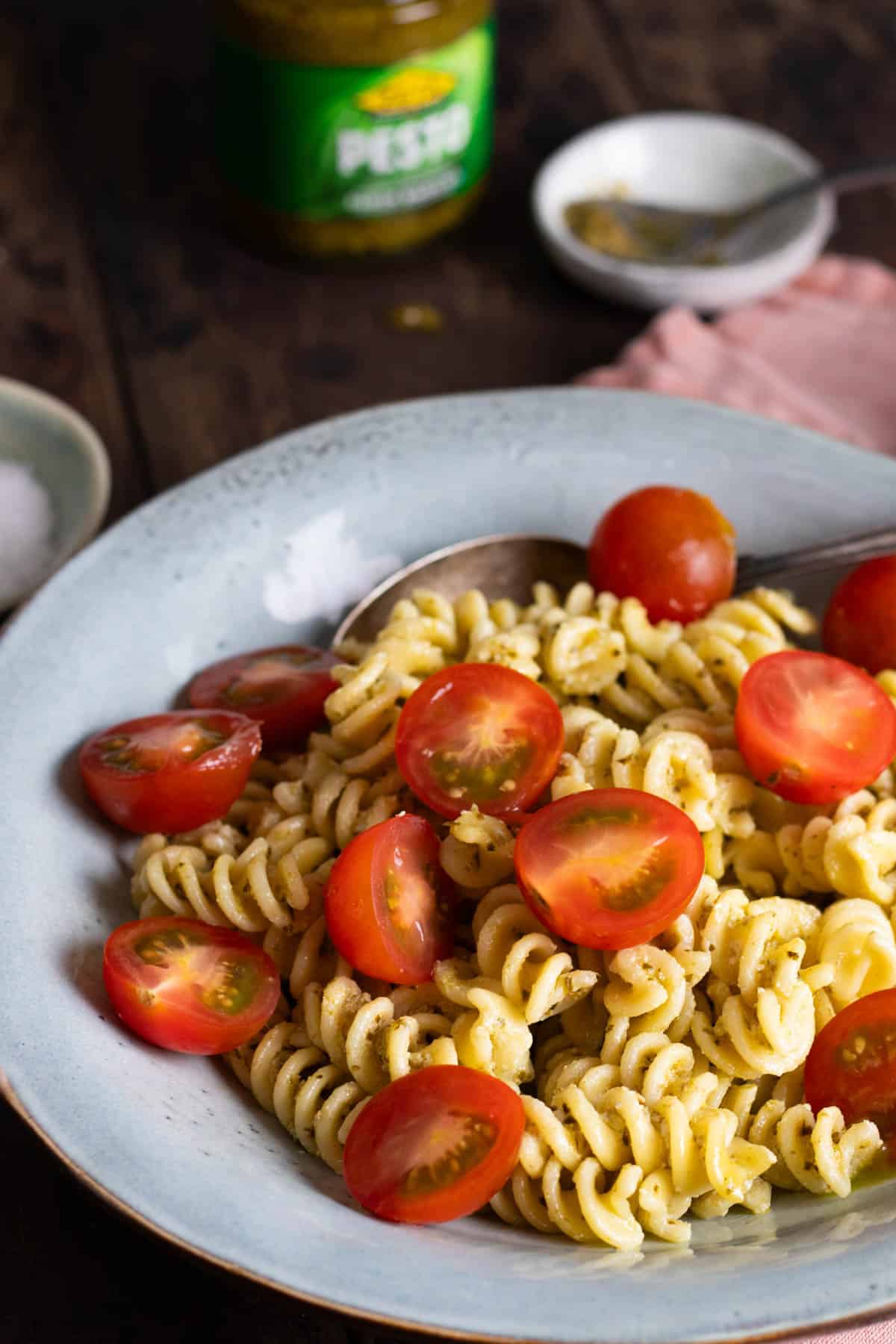 A bowl of creamy pesto pasta topped with cherry tomatoes.