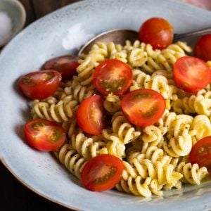 A bowl of creamy pesto pasta topped with cherry tomatoes.