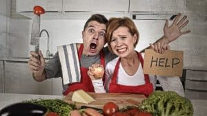 A couple in the kitchen where the woman is holding a sign that says "help".