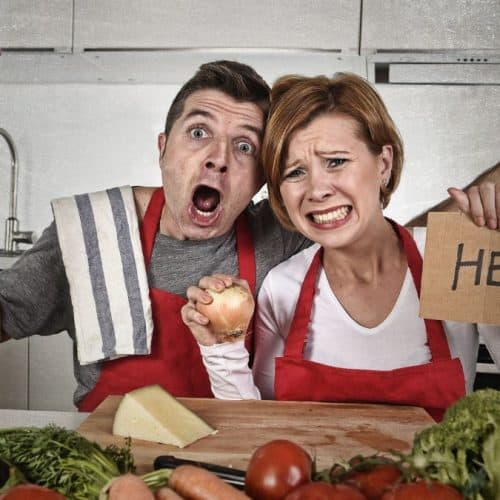 A couple in the kitchen where the woman is holding a sign that says "help".