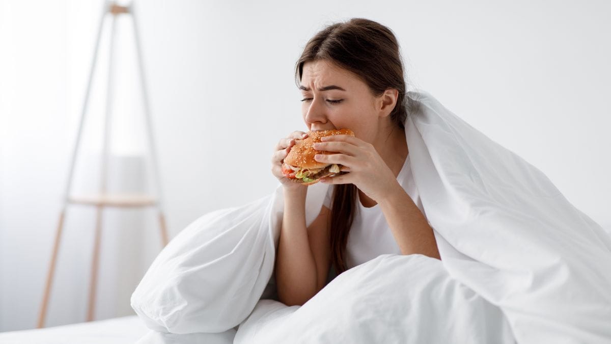 A woman eating a burger in bed.