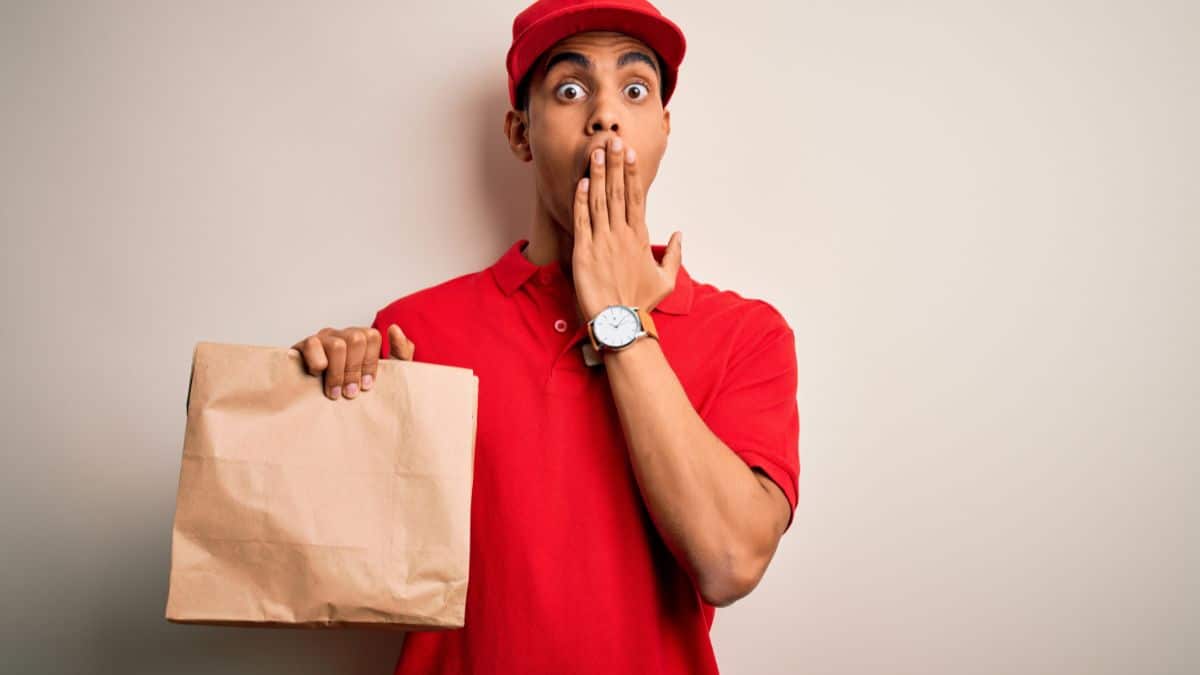 A fast food worker holding a brown bag and looking surprised.