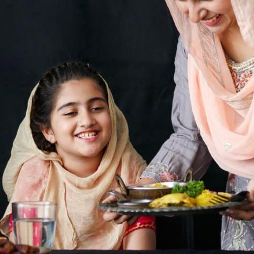 A Pakistani woman serving food to a child.