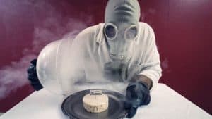 A man in a gas mask holding out a plate with cheese.