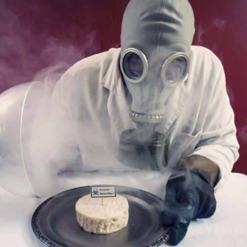 A man in a gas mask holding out a plate with cheese.