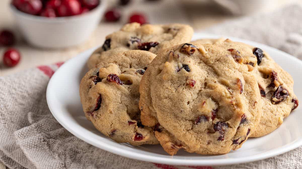Cranberry walnut cookies on a plate with bowl of cranberries in background.