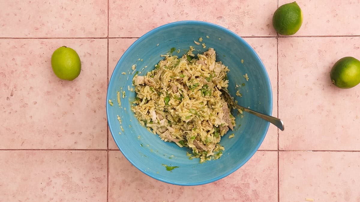 Shredded chicken mixed with cheese and green enchilada sauce, to make filling for enchiladas.