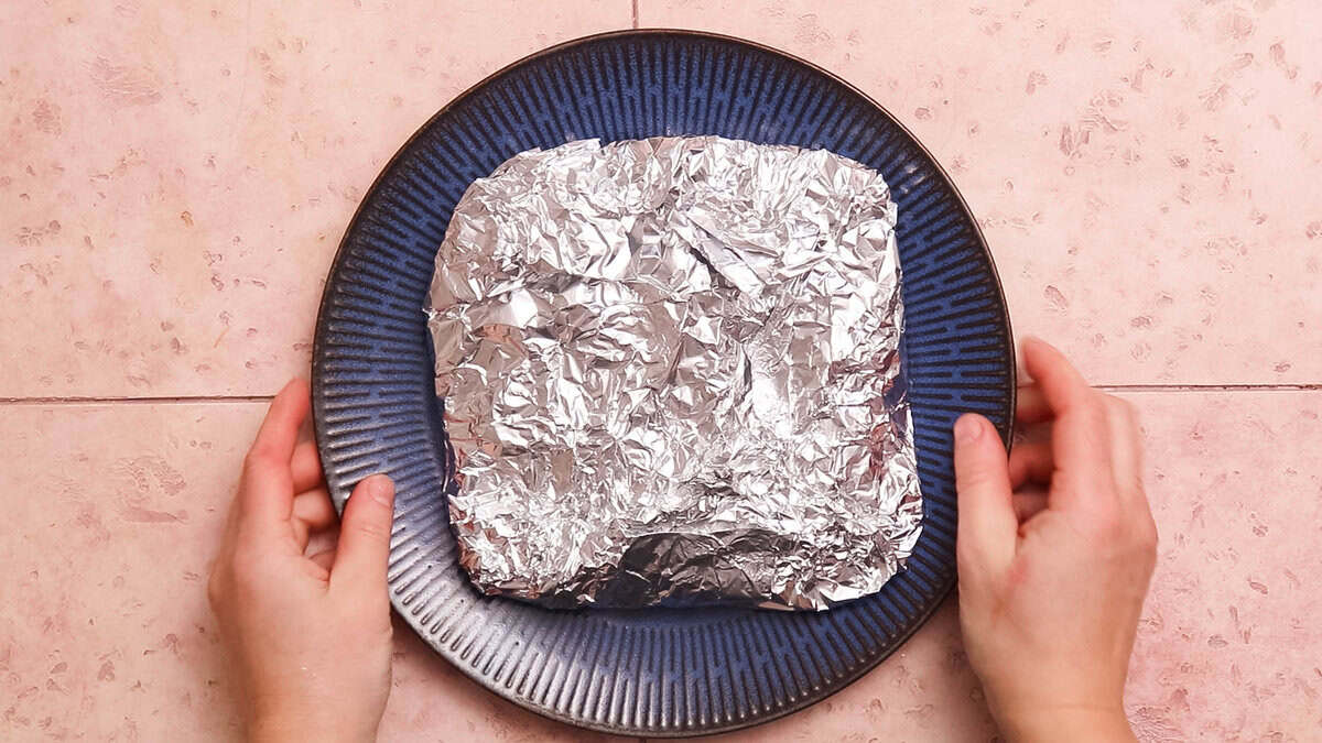Flank steak wrapped in aluminum foil to rest.