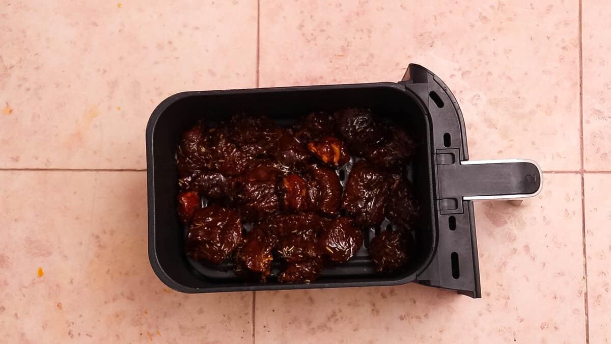 Steak bites in an air fryer basket before cooking.