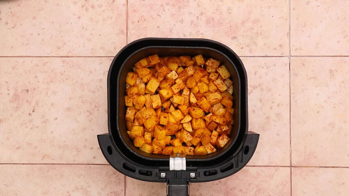 Seasoned breakfast potatoes in an air fryer basket before cooking.