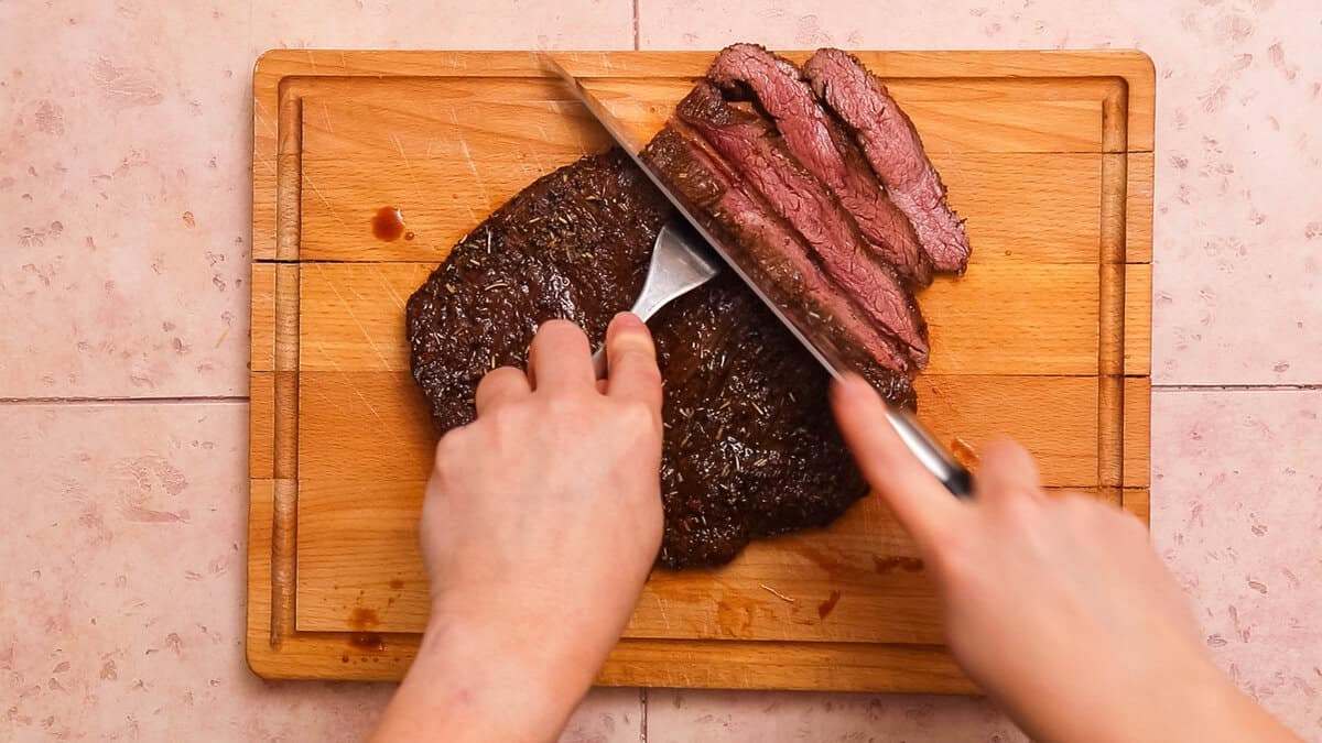 Slicing flank steak or skirt steak on a wooden chopping board.